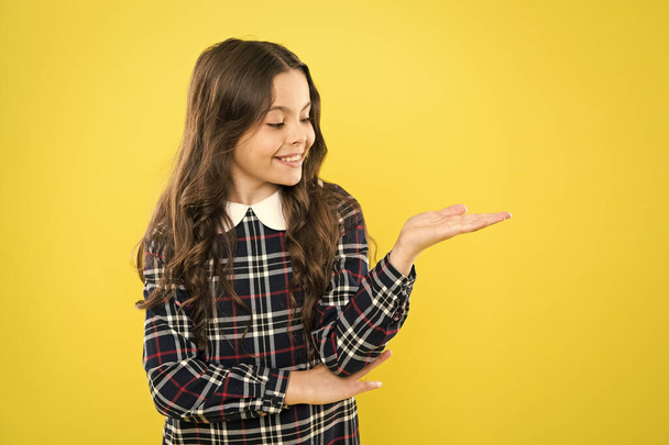 beauty product. kid presenting product. child has long curly hair. after visit to hairdresser. happy schoolgirl in fashion uniform. back to school. small girl classy checkered dress. copy space - Фото, изображение
