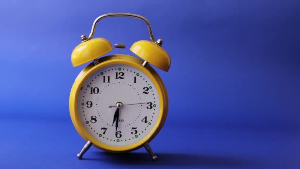 アラームをトリガーする古いレトロな黄色の目覚まし時計。青い背景に隔離された時計のリンギング - 映像、動画