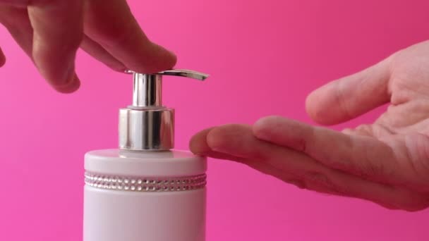 Distributore di spinta a mano e sapone liquido spremuto fino alle dita, colpo di primo piano su uno sfondo rosa - Filmati, video