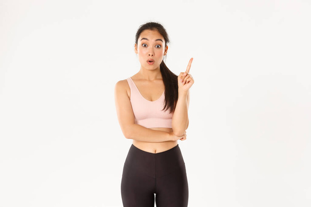 Spor, refah ve aktif yaşam tarzı konsepti. Düşünceli fit ve zayıf Asyalı kızın bir fikri var, sporcu kadın öneriler için işaret parmağını kaldır, egzersiz planı yap, beyaz arka planda dur - Fotoğraf, Görsel