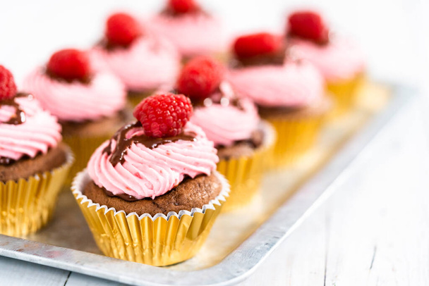 Gourmet chocolate raspberry cupcakes drizzled with chocolate ganache and topped with a fresh raspberry. - Foto, Imagem