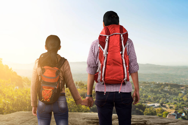 Rear view of Asian couple with backpack looking at mountain view with a blue sky background. World Tourism Day - Foto, Imagen