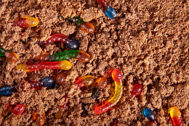 Vermes de goma coloridos e brilhantes variados em chão de bolo de chocolate, comida de festa de halloween, espaço de cópia - Foto, Imagem
