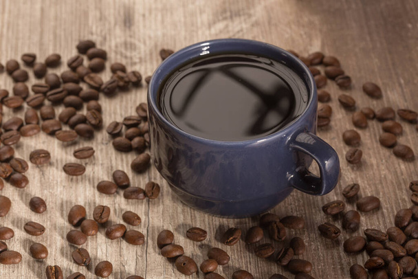 modrý šálek s černou kávou, kolem s rozšířenou kávovou zrno, na dřevěném povrchu, studio - Fotografie, Obrázek