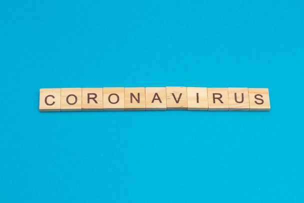 Слово CORONAVIRUS сделано из деревянных кубиков на синем фоне. - Фото, изображение