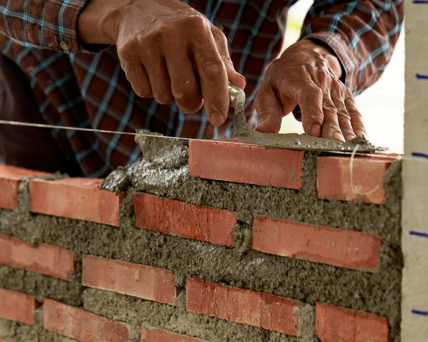 Bricklayer w pracy. Zbliżenie przemysłowych murarzy montujących cegły na placu budowy - Zdjęcie, obraz