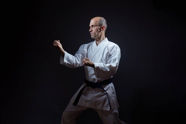 Op een zwarte achtergrond staat een jonge atleet in een karatestand - Foto, afbeelding