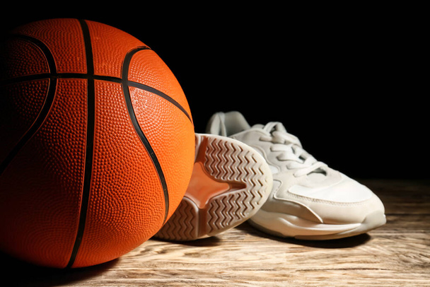Bola para jogar basquete e sapatos na mesa contra fundo escuro - Foto, Imagem
