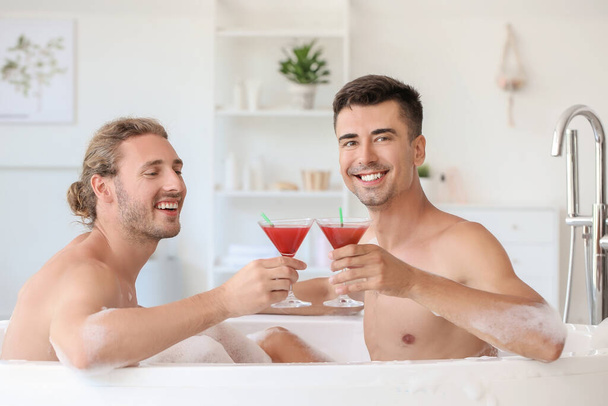 heureux gay couple boire cocktails dans salle de bain - Photo, image