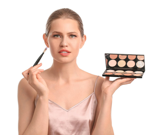 Beautiful young woman with makeup brush and eyeshadows on white background - Fotoğraf, Görsel