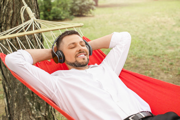Komea liikemies kuuntelee musiikkia rentoutuessaan riippumatossa ulkona - Valokuva, kuva