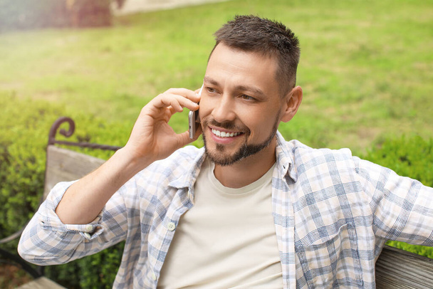 Handsome man talking by phone while relaxing in park - Photo, Image