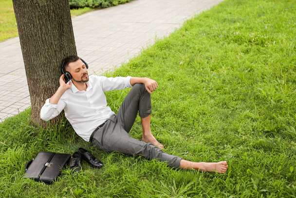 Yakışıklı iş adamı parkta dinlenirken müzik dinliyor. - Fotoğraf, Görsel