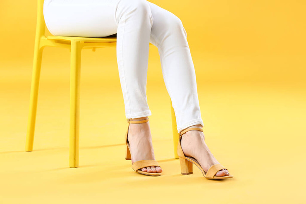 Young woman in stylish shoes sitting on chair against color background - Fotoğraf, Görsel