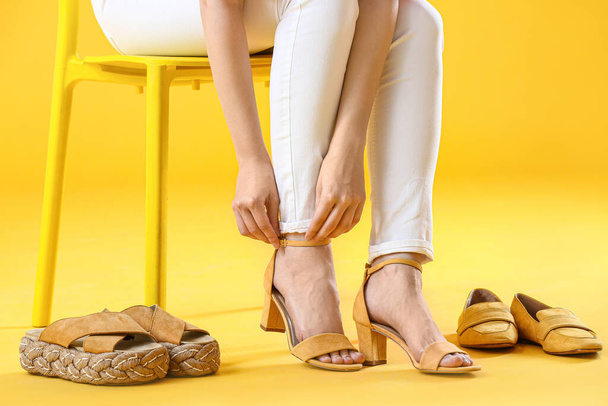 Young woman trying on stylish shoes while sitting on chair against color background - Foto, Imagem