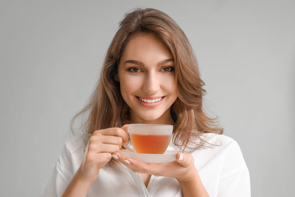 Belle jeune femme avec une tasse de thé sur fond gris - Photo, image
