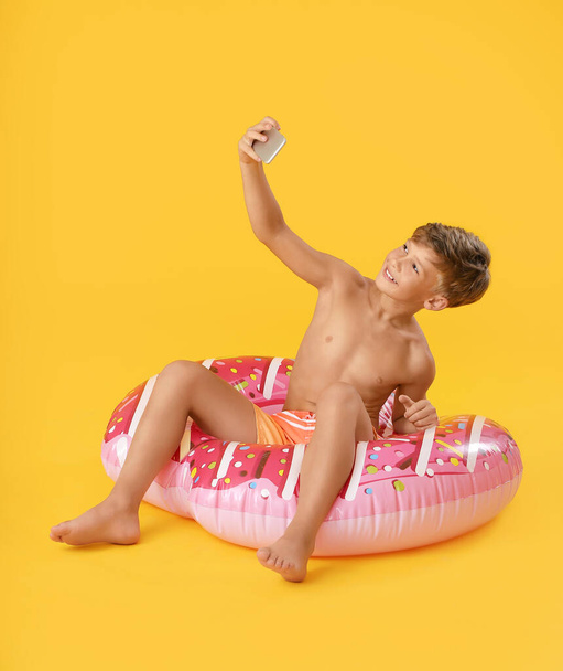 Cute little boy with inflatable ring taking selfie on color background - Photo, Image