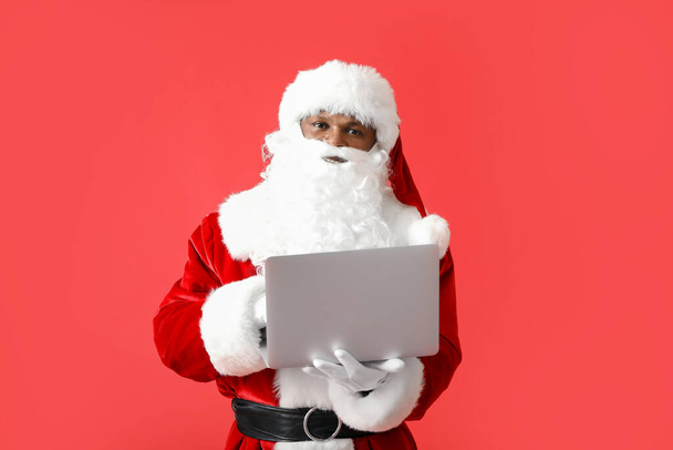 Афро-американский Санта-Клаус с ноутбуком на цветном фоне - Фото, изображение