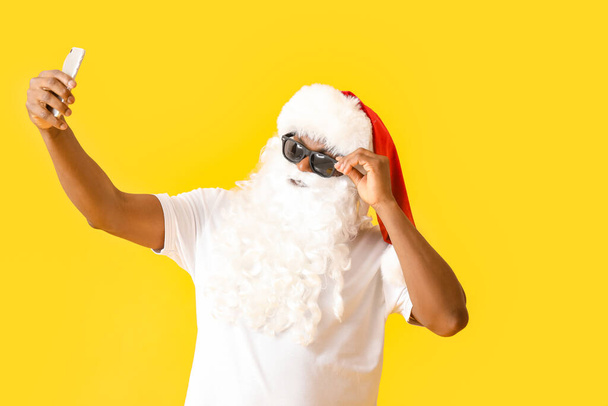 Cool afroamericano Santa Claus tomando selfie sobre fondo de color - Foto, imagen