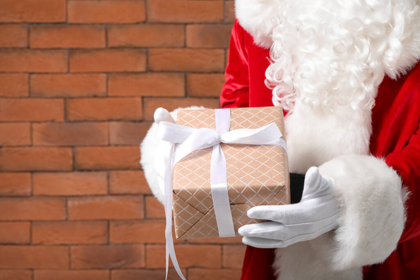 Santa Claus s dárkem na cihlovém pozadí, detailní záběr - Fotografie, Obrázek