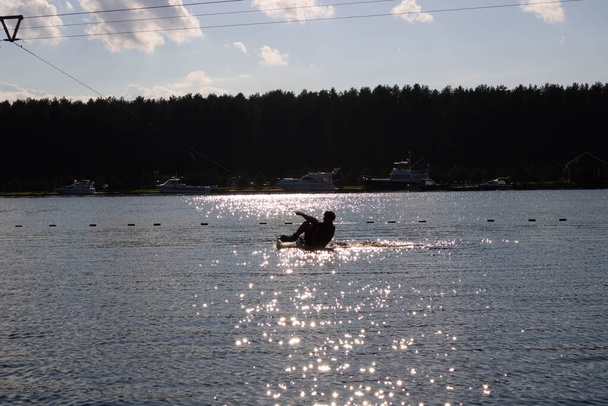 Silueta de esquí acuático moviéndose rápido en salpicaduras de agua al atardecer - Foto, Imagen