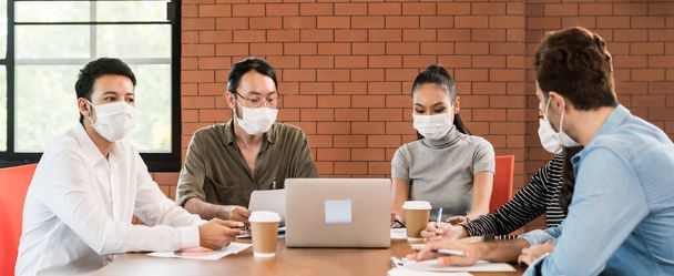 Panorama asian and caucasian business person team meeting brainstorm in meeting room after office reopen, they wear protective face mask as new normal practice to prevent coronavirus infection. - Photo, Image