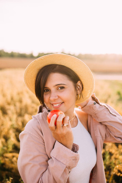 a girl in a straw hat in a field with an apple - Foto, Bild