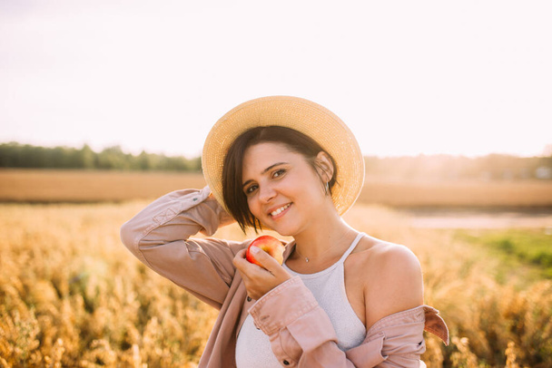 a girl in a straw hat in a field with an apple - Foto, afbeelding