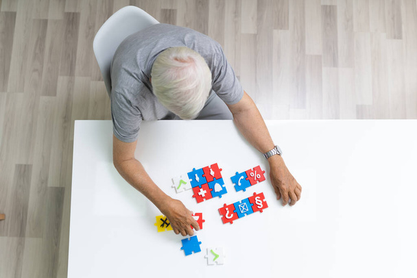 Elder Man Playing Jigsaw Puzzle On Table - 写真・画像