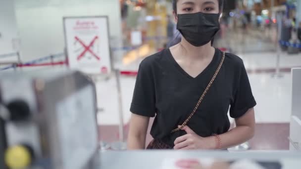 Fiatal ázsiai nő kap repülőjegyet a légitársaságok check-in pulttól a repülőtéri terminálon, beszállókártya, covid-19 járvány, új normál utazási társadalmi távolság, légitársaság légiközlekedési ipar - Felvétel, videó