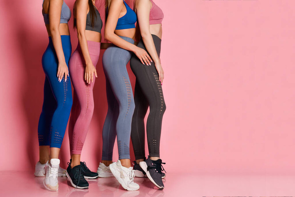 Closeup on legs of standing behind each other athletic women in blue, grey, brown training suits on pink background - Foto, imagen