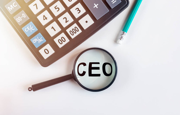 looking at a magnifying glass word acronym: CEO, calculator and pen on white table, top view - Valokuva, kuva