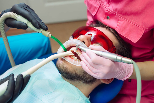 Professional teeth cleaning. Dentist cleans the teeth of a male patient. - Photo, image