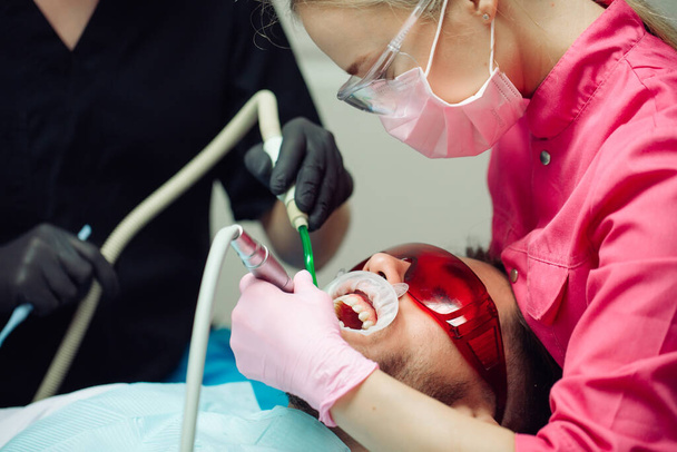 Professional teeth cleaning. Dentist cleans the teeth of a male patient. - Photo, image