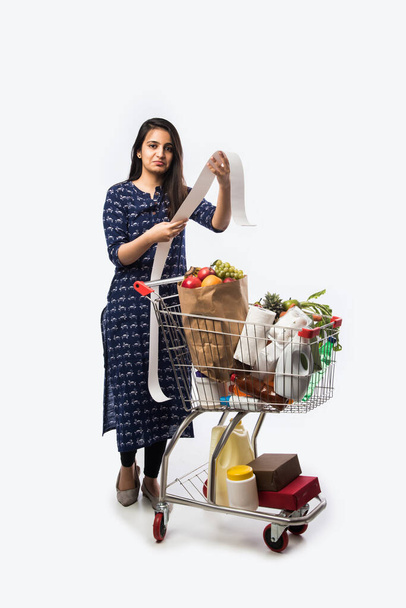 Indian young woman with shopping cart or trolly full of grocery, vegetables and fruits.  Isolated Full length photo over white background - Photo, Image