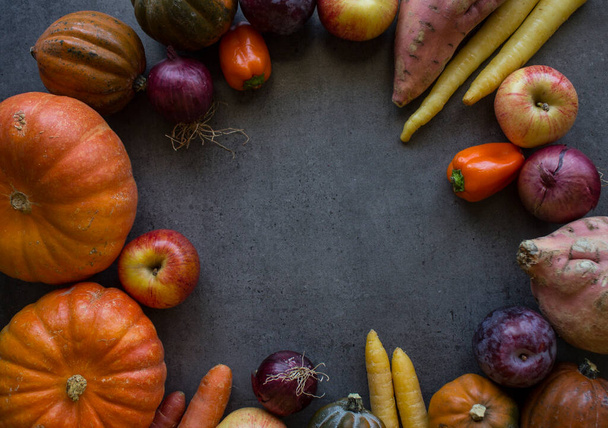 Top view photo of pumpkins, carrots, apples, cherry tomatoes and red onion on grey background with copy space. Colorful frame or border made of fresh autumn vegetables.  - Photo, Image