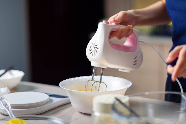 Femme utilisant un mélangeur électrique pour mélanger les ingrédients pour la pâte de sucre, oeufs battus, beurre et farine tout en faisant des biscuits dans la cuisine à la maison gros plan - Photo, image