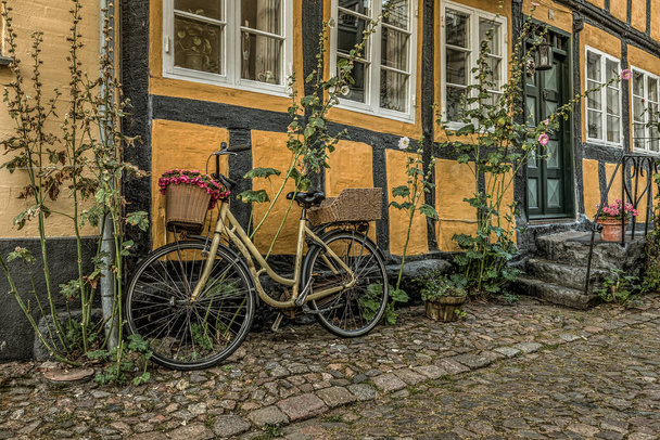 bici amarilla apoyada en una pared amarilla de entramado de madera con hollyhocks, Faaborg, Dinamarca, 17 de agosto de 2020 - Foto, imagen