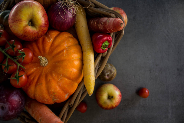 バスケットの新鮮な庭の野菜:カボチャ、リンゴ、ニンジン、チェリートマトと赤玉ねぎ。秋の収穫写真。濃い灰色の背景.  - 写真・画像