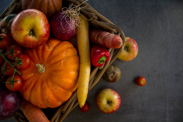 バスケットの新鮮な庭の野菜:カボチャ、リンゴ、ニンジン、チェリートマトと赤玉ねぎ。秋の収穫写真。濃い灰色の背景.  - 写真・画像