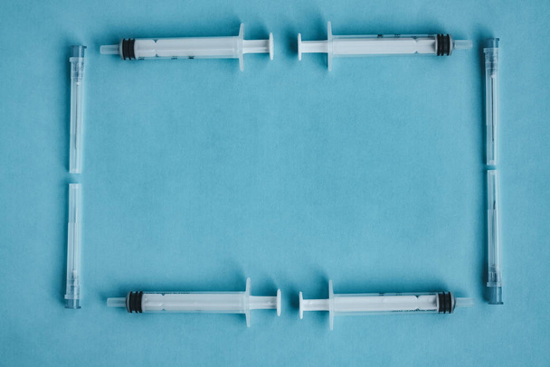 A frame of syringes and needles isolated on a blue background. Coronavirus vaccine. Pandemic and treatment concept. Blood test. Mock up,space for text - 写真・画像