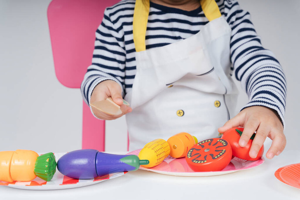 閉じる-野菜にナイフスライスを使用して台所でエプロン調理食品を身に着けている子供. - 写真・画像