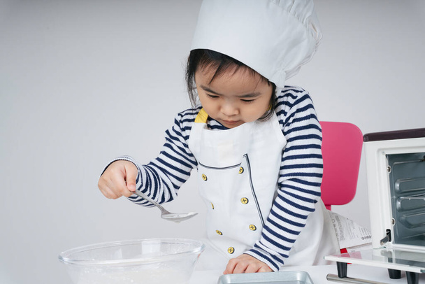 bastante asiático tailandés niño jugar papel como un chef poner mixta harina en hornear plato - Foto, Imagen