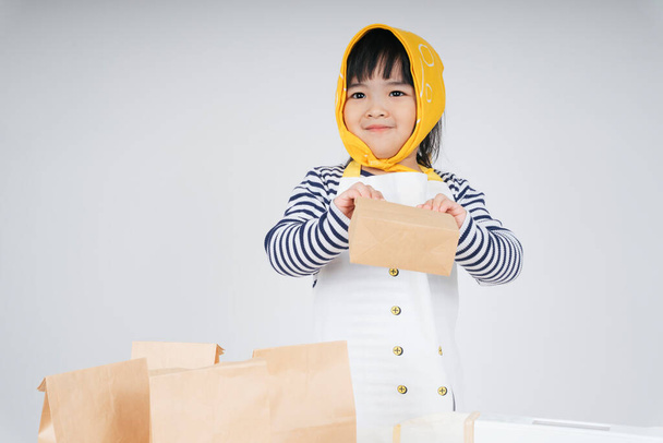 dość Azji tajski dzieciak grać rolę jako kelnerka noszenie żółty bandaż pakowania żywności w papierowej torbie. - Zdjęcie, obraz