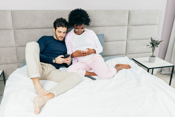 American guy sharing photos with his lovely African girlfriend in bedroom - Valokuva, kuva