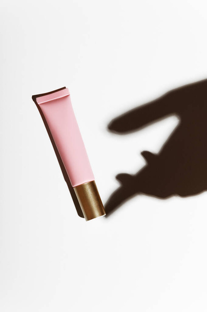 Shadow hands with a pink tube of moisturizing scream on a white background. The attribute of facial and hand care. Tonal, concealer for woman skin - Fotografie, Obrázek