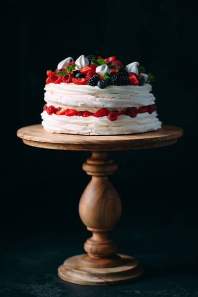Fruit cake. Cake decorated with berries on a wooden stand on a black background. - Foto, afbeelding