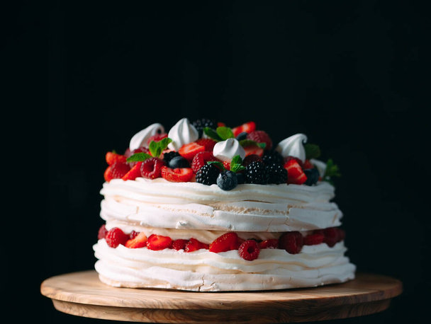 Fruit cake. Cake decorated with berries on a wooden stand on a black background. - Foto, imagen