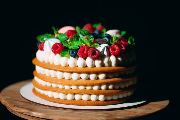 Fruit cake. Cake decorated with berries on a wooden stand on a black background. - Photo, image