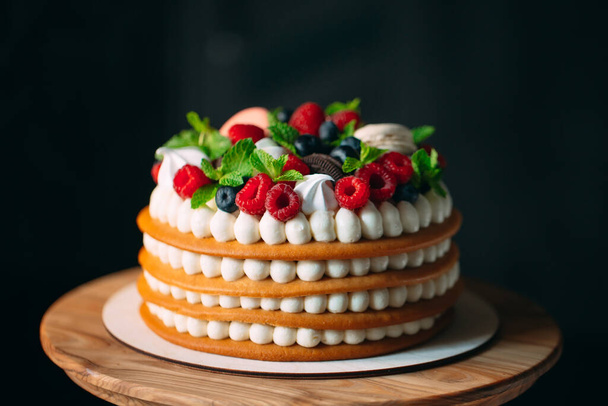 Fruit cake. Cake decorated with berries on a wooden stand on a black background. - Foto, Imagem
